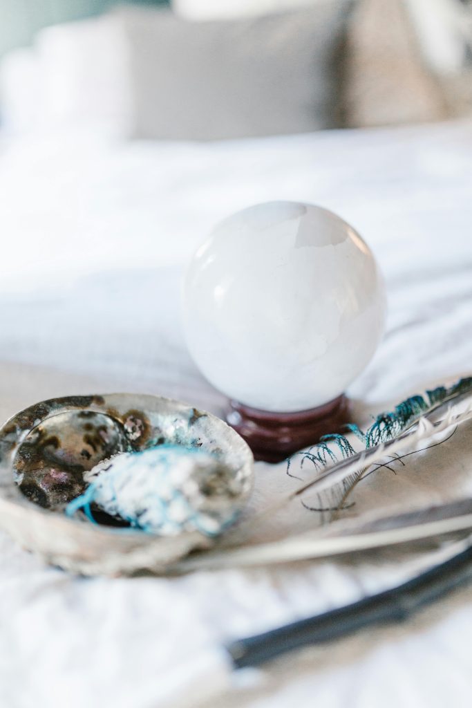 pexels-photo-6806379-6806379 Crystal ball and feather with smudging tools on a soft surface, ideal for spiritual and mystical themes.
